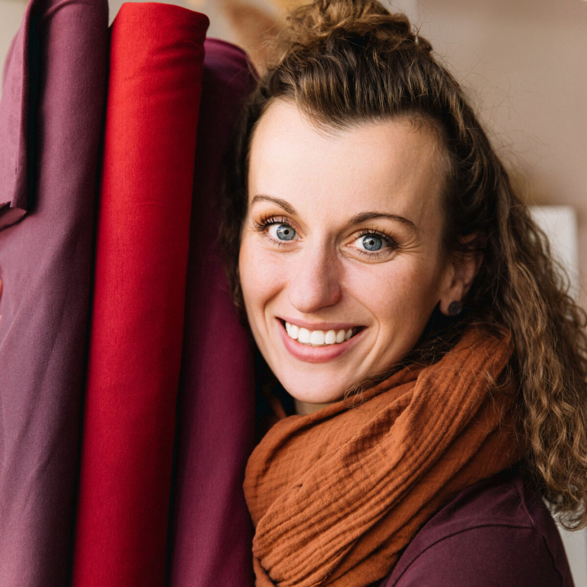 Delighted woman with curly hair bursting into laughter, holding vibrant fabric rolls